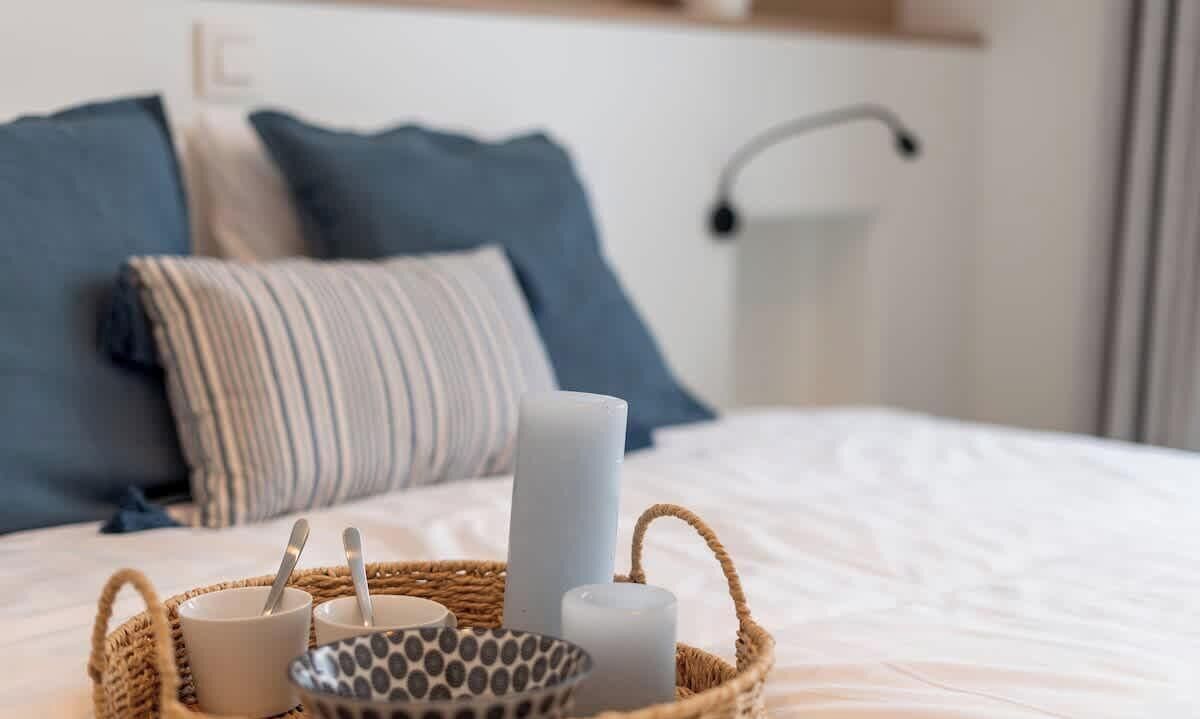 Een net opgemaakt bed met een witte deken, een gestreept kussen en een blauw kussen.