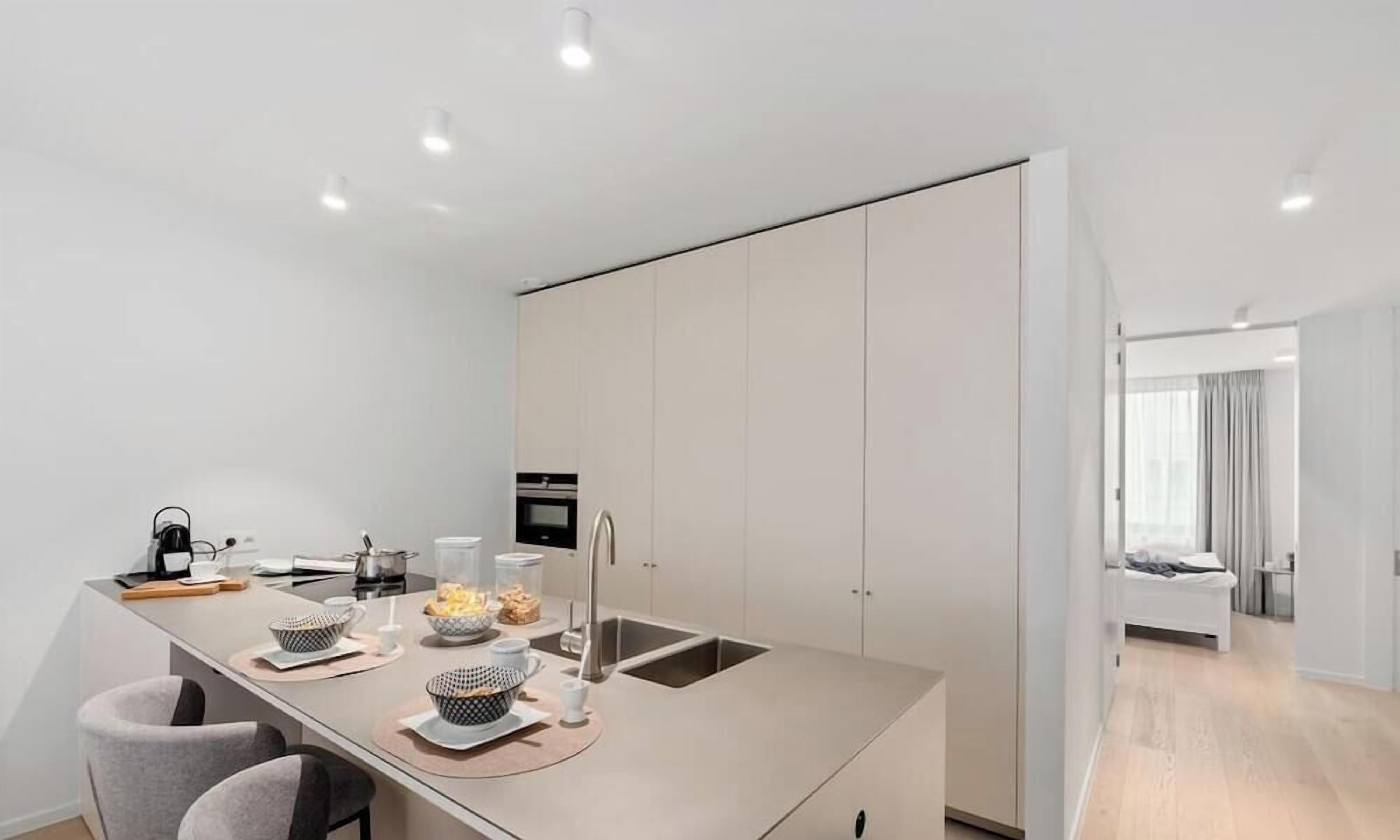 A modern kitchen with a central island, built-in appliances, and a dining area with chairs.