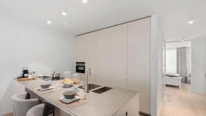 A modern kitchen with a central island, built-in appliances, and a dining area with chairs. - Duin & Kust Residence - 50 metres from the beach, promenade and dunes (Oostduinkerke)