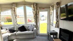 Un salon avec un canapé, un téléviseur et une fenêtre avec des rideaux.