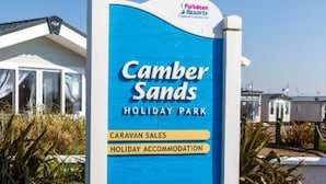 Une enseigne indiquant le parc de vacances de Camber Sands, qui propose des équipements tels qu’un restaurant, un bar avec spectacles, des piscines intérieures chauffées et un espace de vente de caravanes.