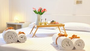 Ein ordentlich bezogenes Bett, gerollte Handtücher, ein Tablett mit Getränken und Gebäck sowie eine Vase mit Blumen.