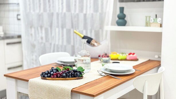 Une table à manger avec une bouteille, un bol de fruits rouges et des assiettes.
