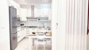 Une cuisine moderne avec des meubles blancs, un réfrigérateur en acier inoxydable, un four à micro-ondes et une cuisinière à gaz.
