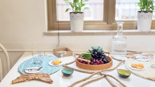 A dining table with a woven placemat, a glass of water, a bottle of water, a basket of grapes, and a plate with food. - Cà 4 Nevodi Chiara by Ca-Sa Check (Chioggia)