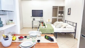 A modern hotel room with a bed, a TV, a desk, and a dining area set with plates, glasses, and a bowl of fruit. - Cà 4 Nevodi Chiara by Ca-Sa Check (Chioggia)