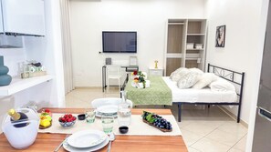 Ein modernes Hotelzimmer mit Bett, Fernseher, Schreibtisch und Essbereich, gedeckt mit Tellern, Gläsern und einer Obstschale.
