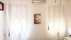 A room with white curtains, a wall-mounted air conditioner, and a framed artwork. - Cà 4 Nevodi Chiara by Ca-Sa Check (Chioggia)