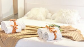 Un lit bien fait, avec des serviettes blanches roulées et attachées par des rubans bruns, une couverture beige et de moelleux oreillers blancs.