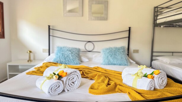 Un lit bien fait, avec des serviettes pliées, une couverture jaune et des fleurs décoratives.