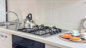 Une cuisine équipée d’une cuisinière à gaz, d’une bouilloire, d’un évier et d’un coin repas pour le petit-déjeuner avec des viennoiseries.