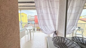 Un balcon avec des chaises blanches, un panier en osier et une vue sur les immebles.
