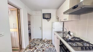 Une cuisine compacte avec un dosseret carrelé, une cuisinière à gaz encastrée, un réfrigérateur et un téléviseur à écran plat fixé au mur.