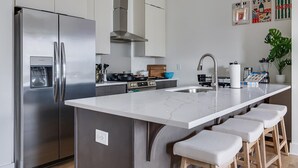 Et moderne køkken med et rustfrit stål køleskab, en central ø med barstole, en gas komfur og en vask.