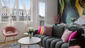 En moderne stue med sofa, rundt sofabord, en lyserød stol og et stort abstrakt billede på væggen.