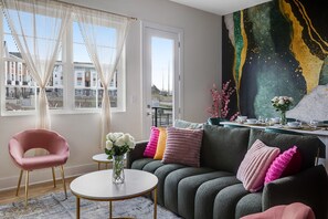 A modern living room with a sofa, a round coffee table, a pink chair, and a large abstract painting on the wall. - {NEW} Green Gem:Rooftop, Hot Tub, Arcade Games, Pool Table, Near Broadway - B (Nashville)