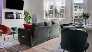En moderne stue med sofa, spisebord og fjernsyn monteret på væggen.