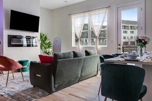 A modern living room with a sofa, a dining table set, and a TV mounted on the wall. - {NEW} Green Gem:Rooftop, Hot Tub, Arcade Games, Pool Table, Near Broadway - B (Nashville)