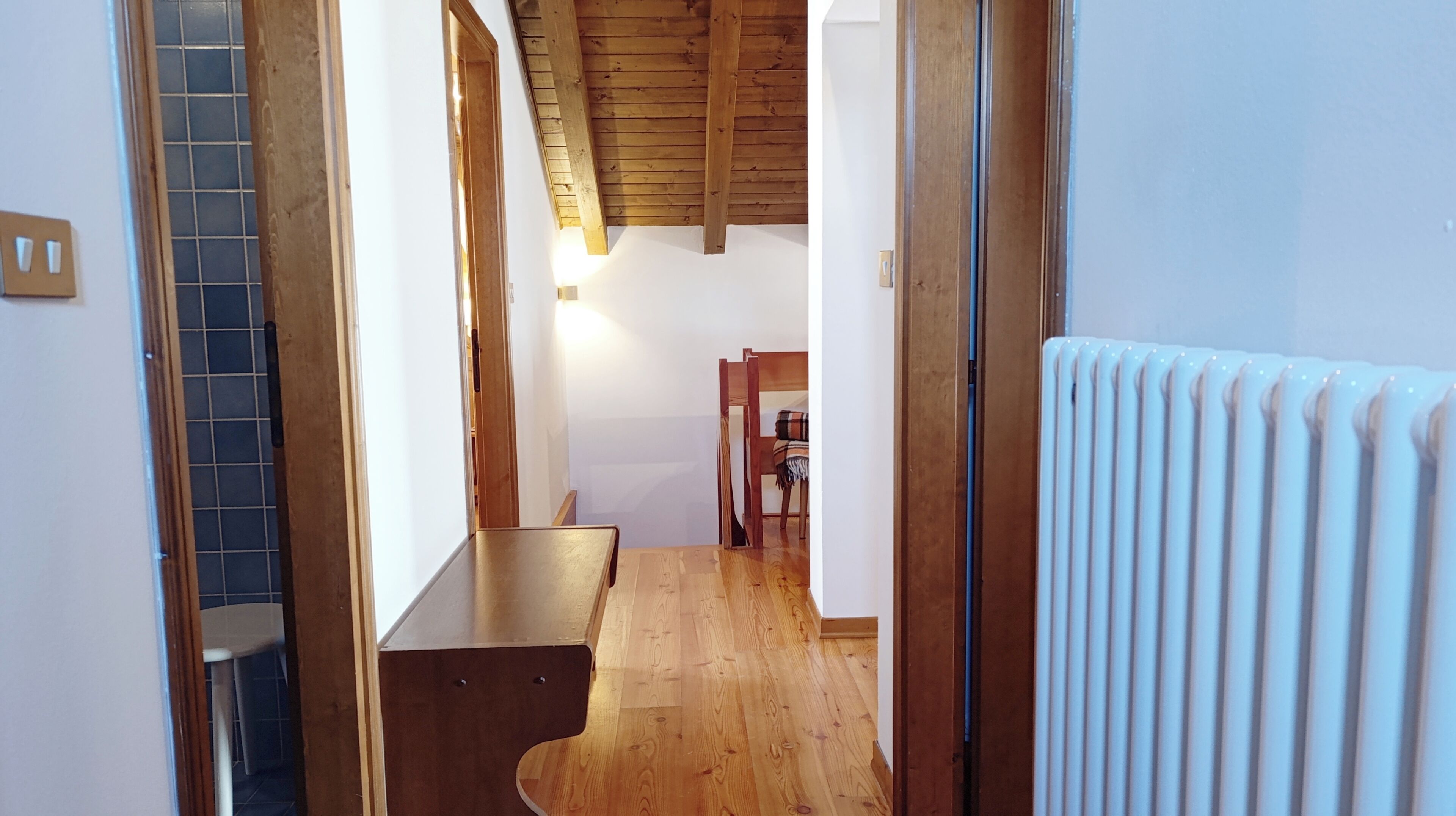 Un couloir étroit avec un plancher en bois, un radiateur et une chaise au fond.