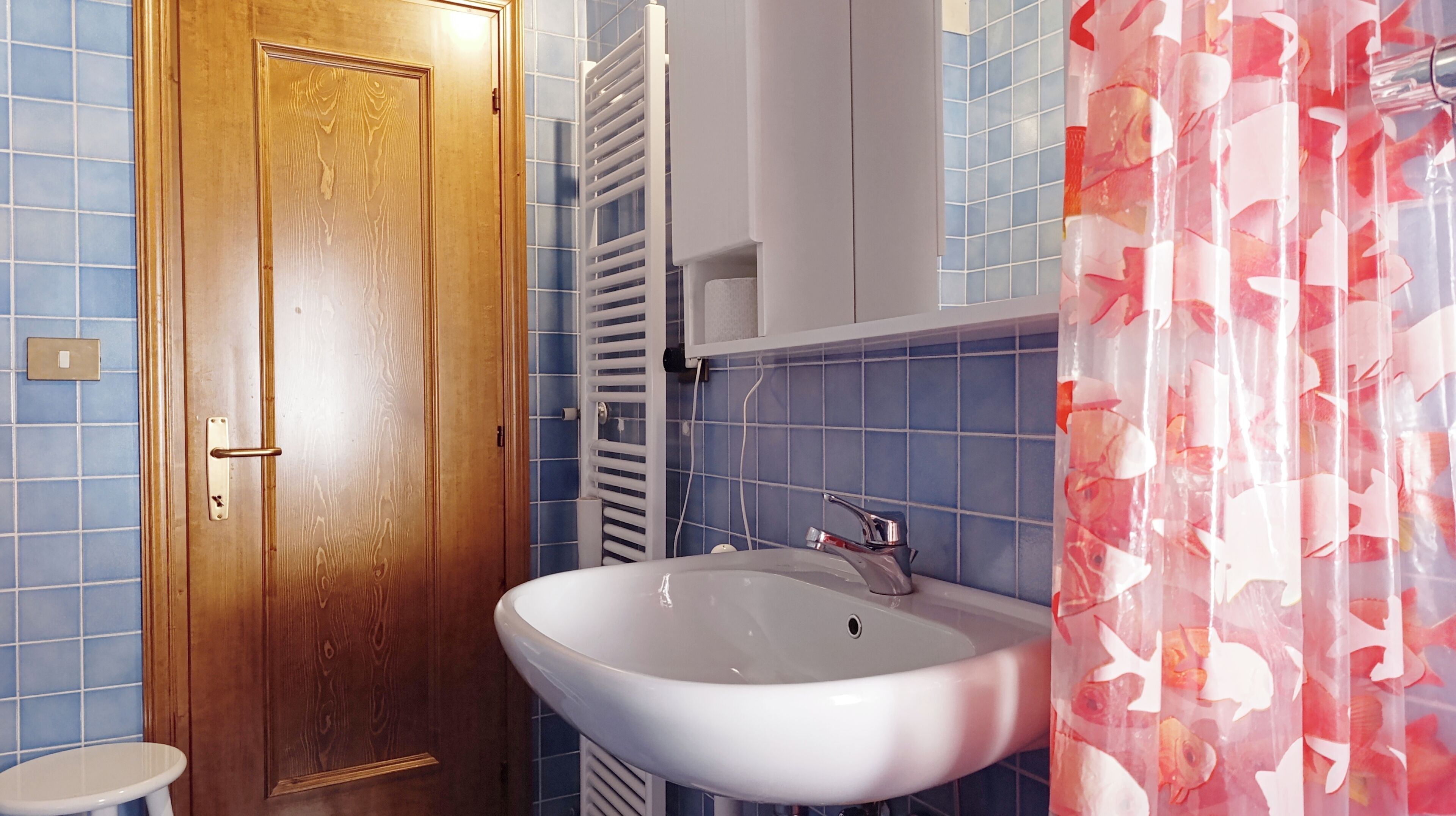 A bathroom with a wooden door, a white sink, a towel rack, and a shower curtain with a floral pattern.