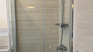 Une douche fermée par des parois en verre, dotée d’un pommeau de douche à main et d’un robinet fixé au mur.