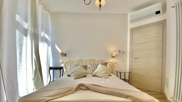Une chambre à coucher avec un lit, des tables de chevet, une lampe, une porte et une fenêtre avec des rideaux.