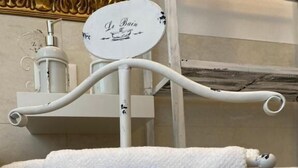 Une salle de bain avec une serviette blanche suspendue à un porte-serviettes, un distributeur de savon et une pancarte sur laquelle est écrit « Le Bain ».