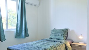 Un letto singolo con una coperta a motivi, un comodino con una lampada e una finestra con tende.