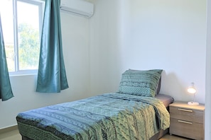 Un lit simple avec une couvre-lit à motifs, une table de chevet avec une lampe et une fenêtre avec des rideaux.