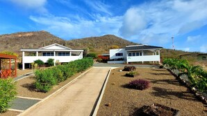Una moderna casa a due piani con vialetto che conduce a un ingresso sorvegliato, circondata da giardini curati e colline sullo sfondo.