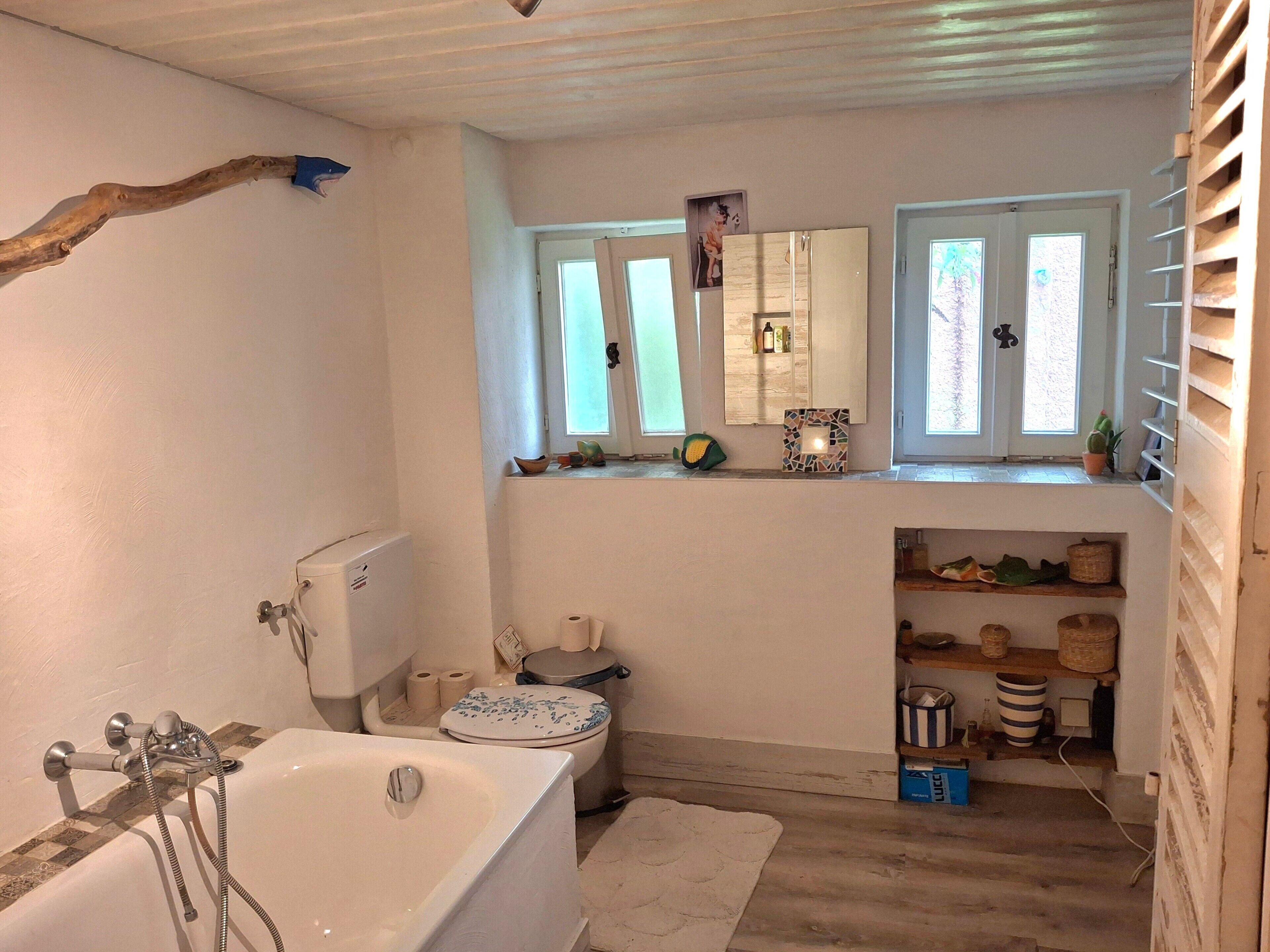 Un baño con bañera, inodoro y un estante con diversos objetos.