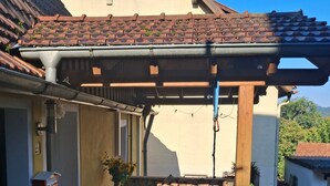 A covered patio area with a table and chairs, a stone wall, and a wooden pergola structure. - Holiday Home 'Charming' with Shared Terrace and Wi-Fi (Neckargemünd)