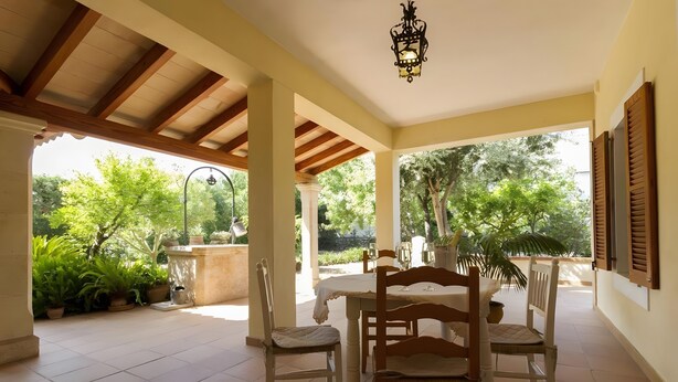 A covered patio with a table set for two, surrounded by chairs, and a hanging light fixture. - Villa 'Panada' with Private Pool, Wi-Fi, and Air Conditioning (Pollença)