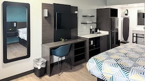 A compact hotel room with a bed, a desk, a chair, a mirror, a TV, a coffee maker, a microwave, and a refrigerator. - Studio 6 Suites Lexington, Kentucky (Lexington)