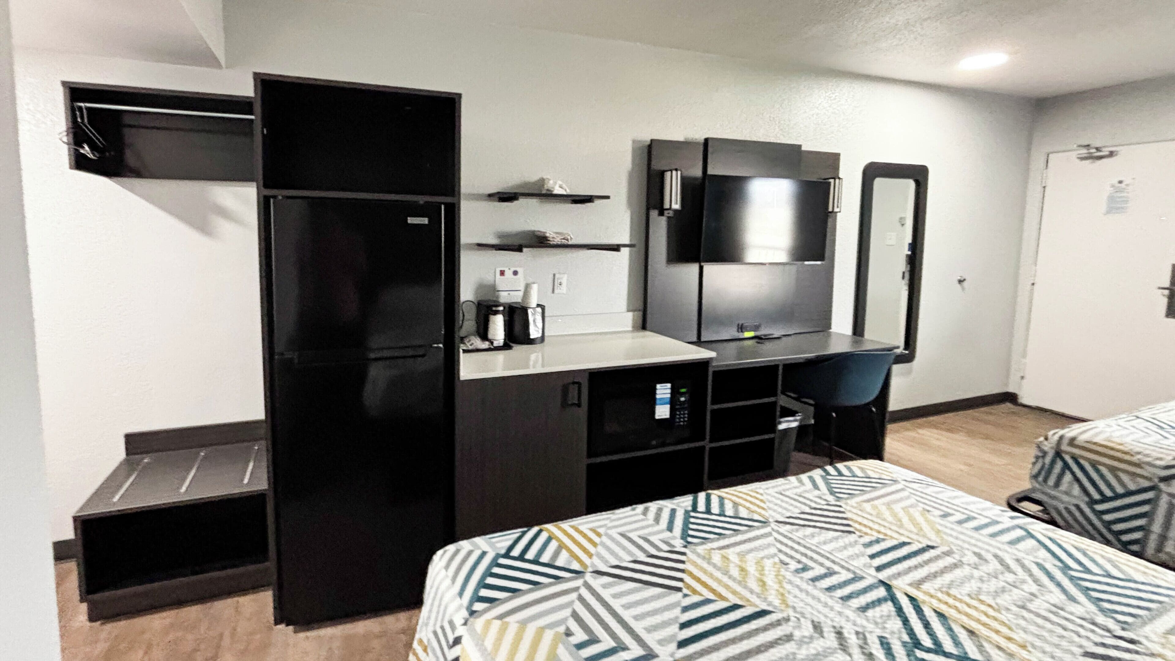 Une chambre d’hôtel équipée d’un lit, d’un bureau avec un ordinateur, d’un réfrigérateur, d’un four à micro-ondes, d’une machine à café et d’un miroir.