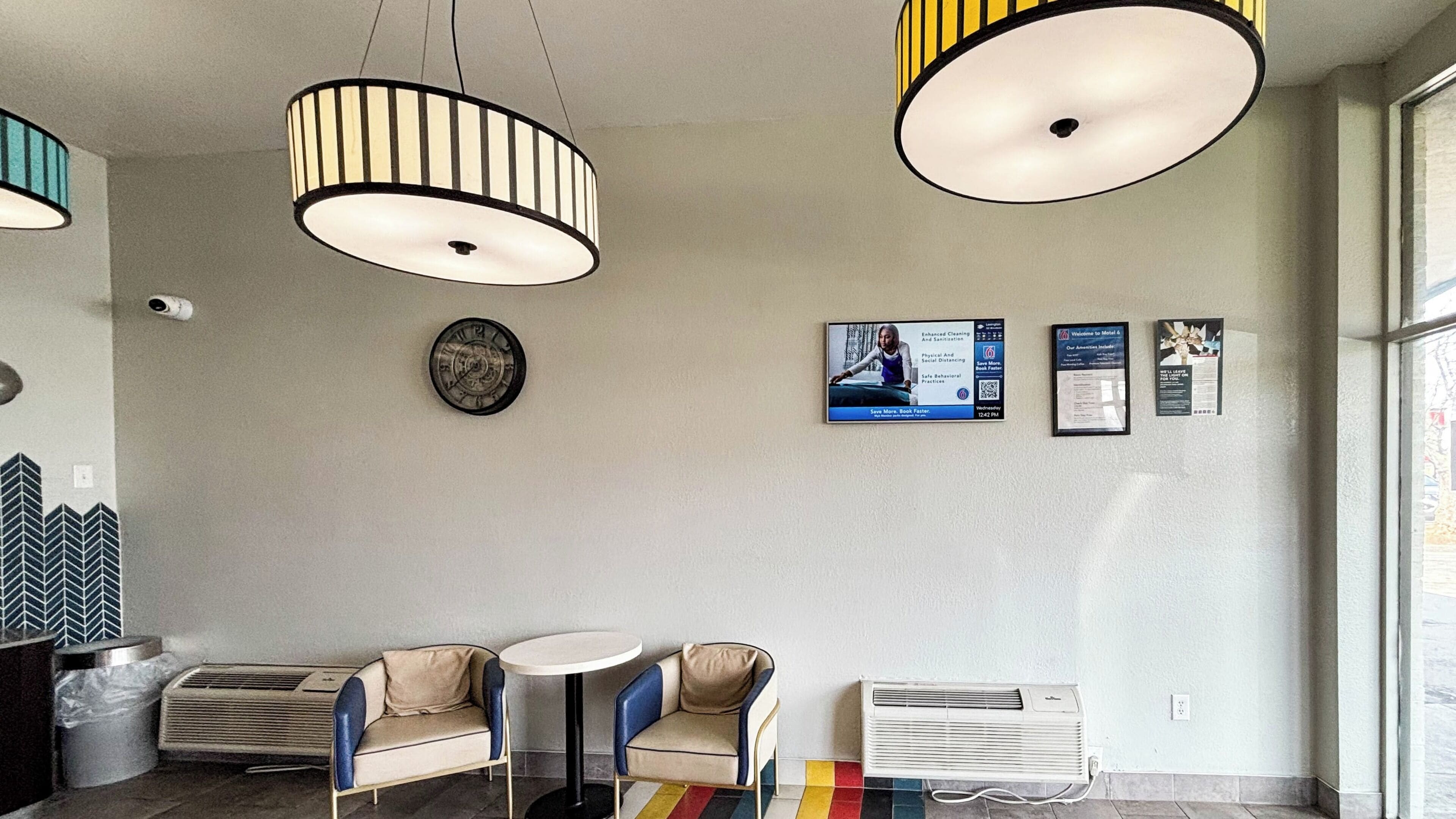A modern interior with two round tables, chairs, a clock, and wall-mounted informational posters.