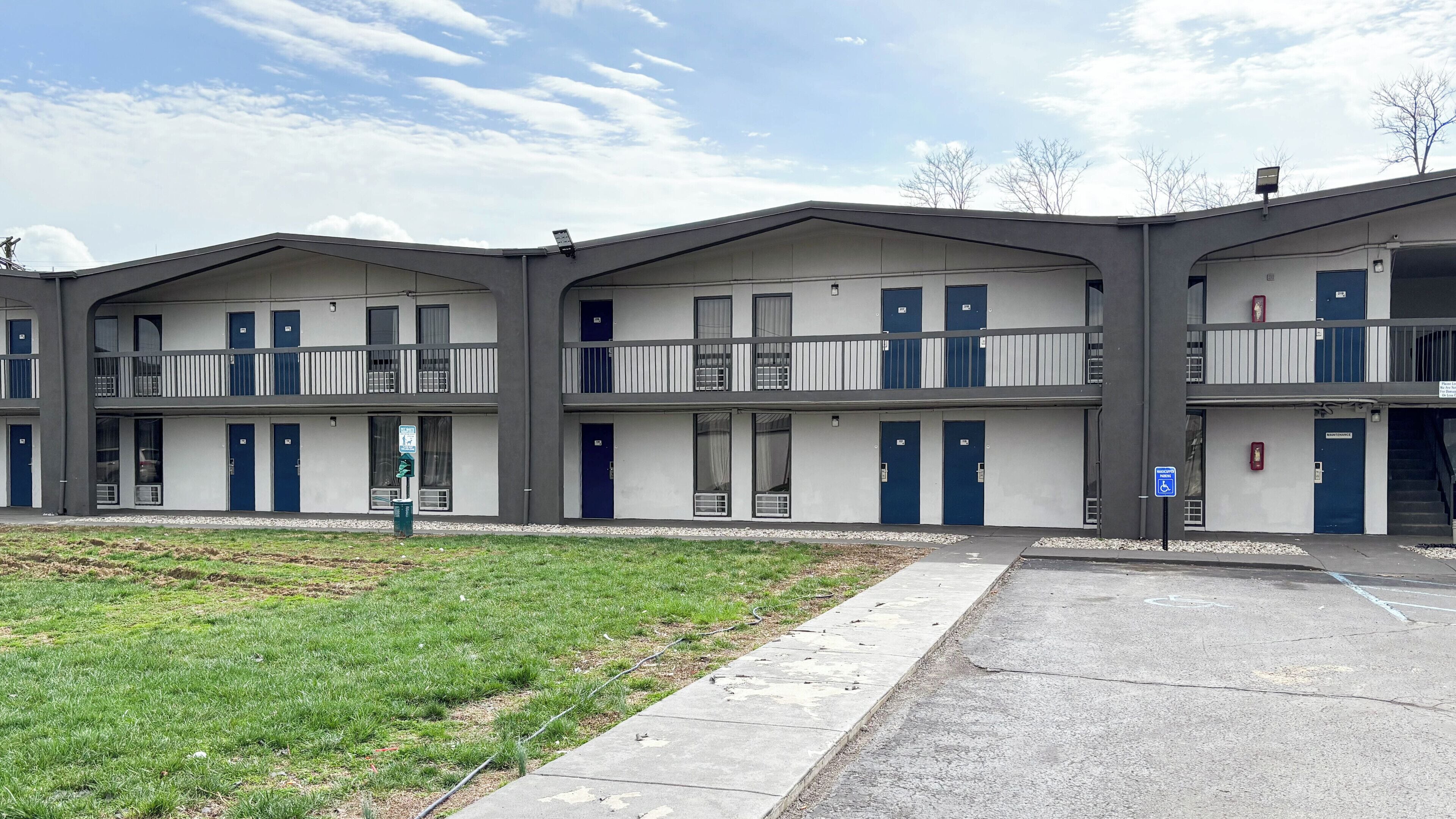 Un motel de varios pisos con techo plano, balcones y un área de estacionamiento.