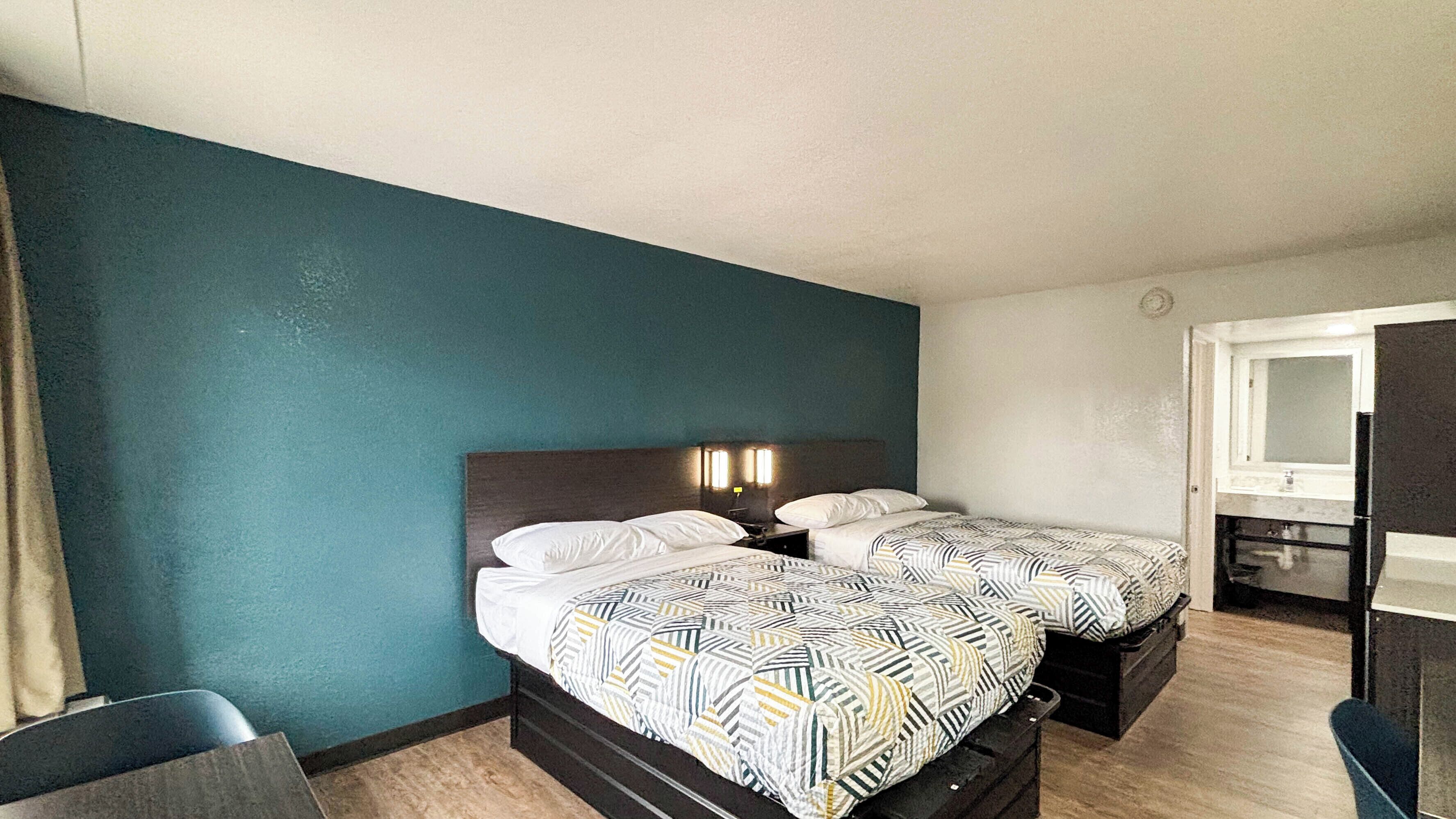 A hotel room with two beds, a desk, a chair, and a mirror.