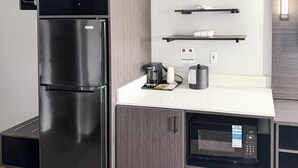 A kitchen with a stainless steel refrigerator, a coffee maker, a microwave, and a small shelf with a towel. - Studio 6 Suites Lexington, Kentucky (Lexington)