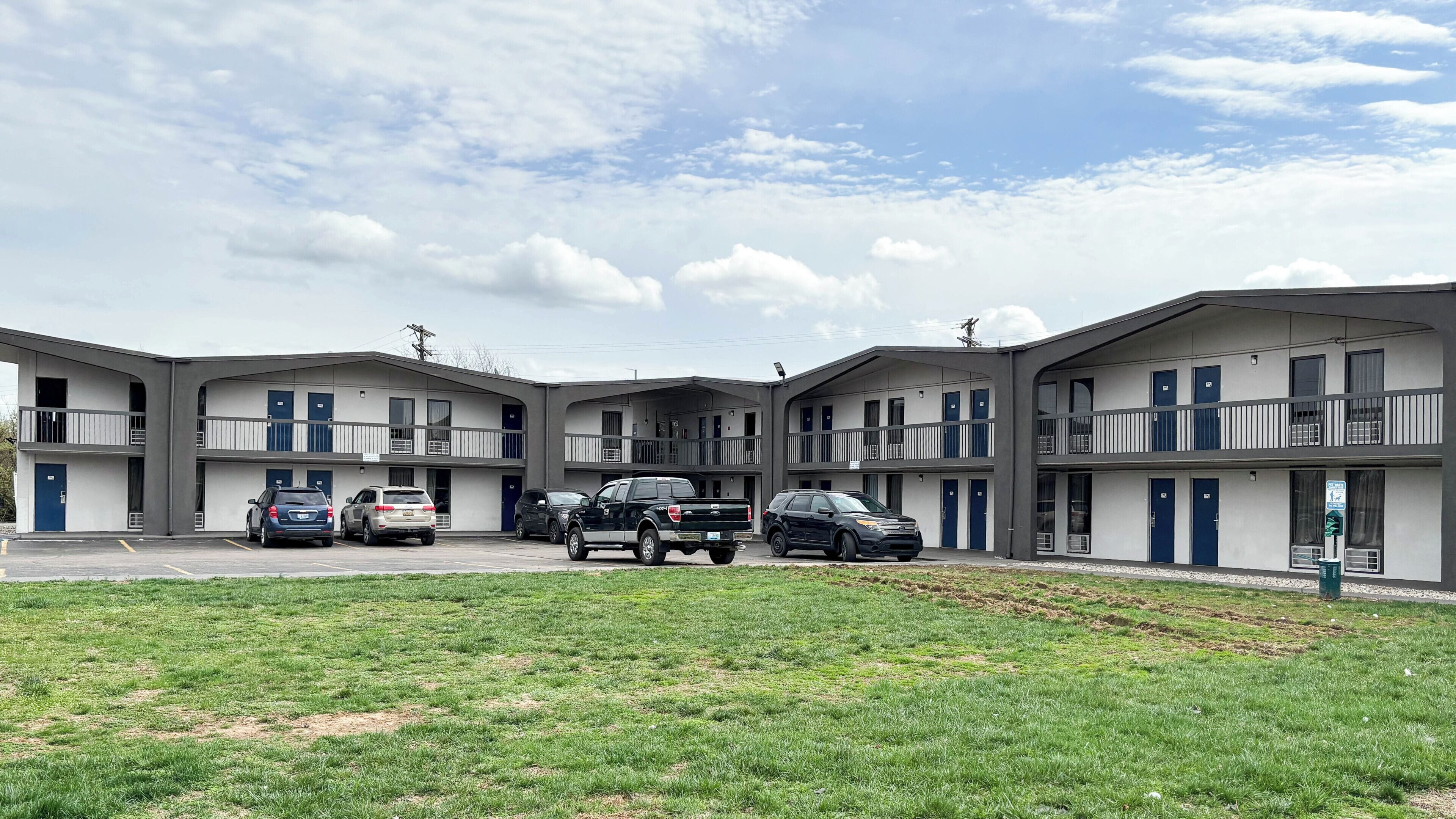 A motel with multiple two-story buildings, parking area, and a grassy front lawn.