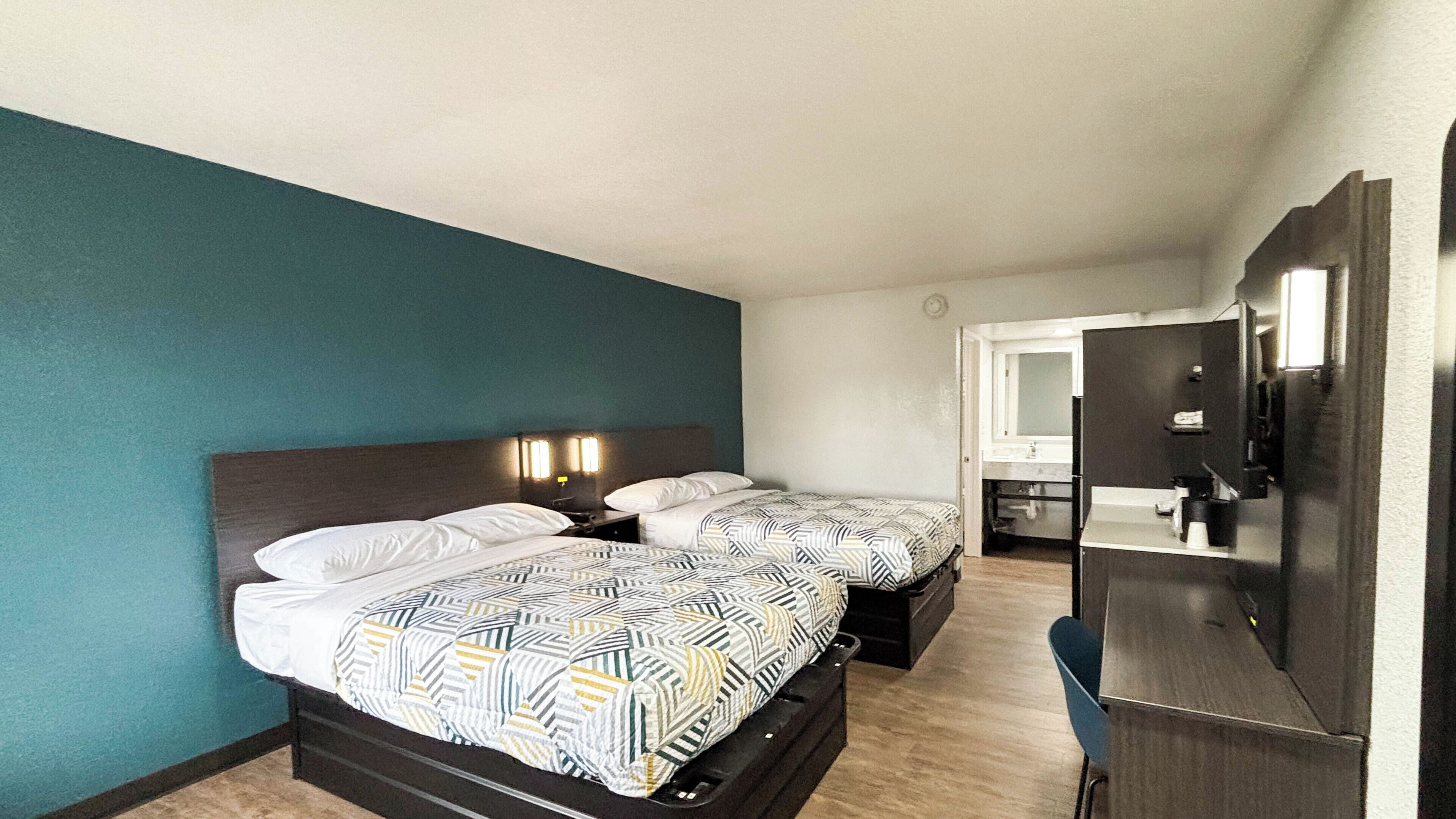 Una habitación de hotel con dos camas, un escritorio, un espejo y una puerta que da a un baño.