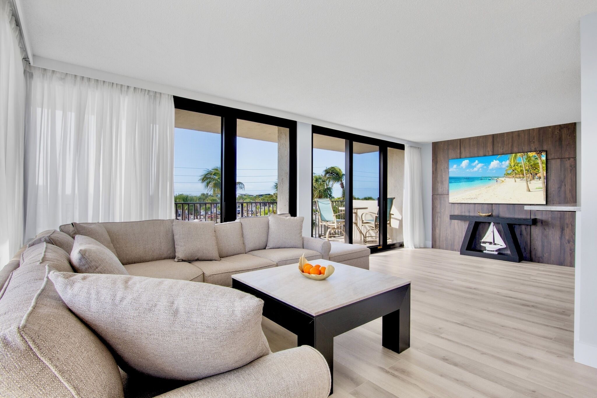 A modern living room with a sectional sofa, a coffee table, and a flat-screen TV mounted on a wooden wall.