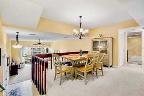 A dining area with a table set for four, a chandelier, and a view into a living room. - Our House at the Beach C-114 (Siesta Key)