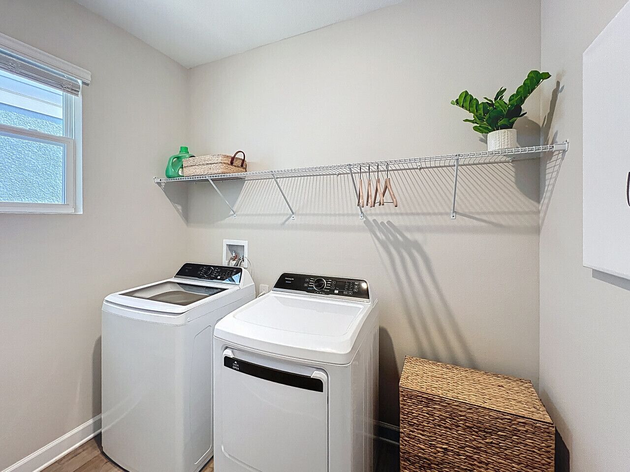A laundry room with two front-loading washing machines, a drying rack, and a small shelf with a plant.