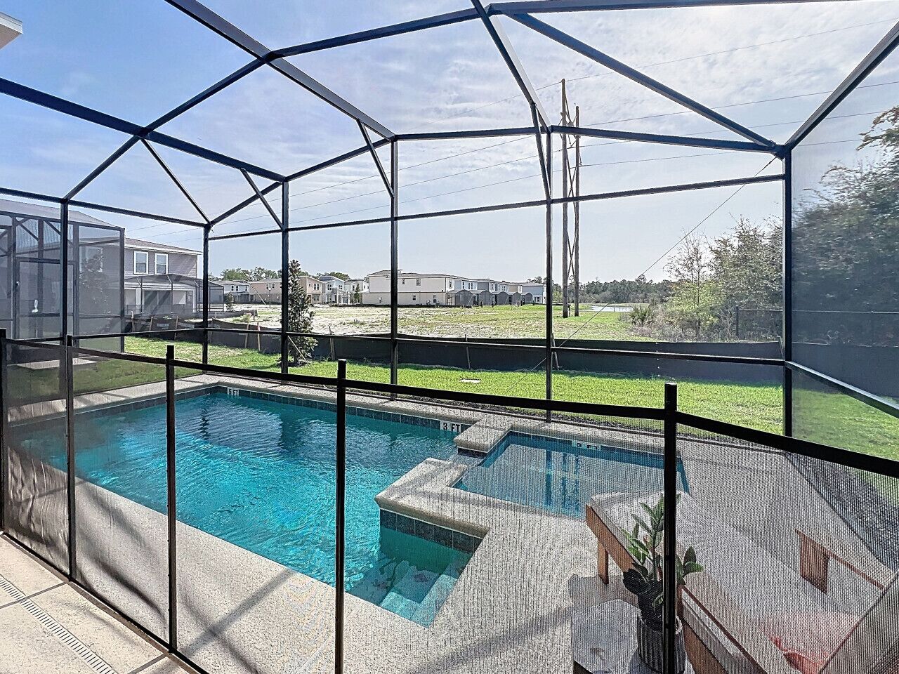 A swimming pool with a glass enclosure, surrounded by a grassy area and residential buildings in the background.