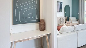 Ein Zimmer mit weißem Schreibtisch, einer Tafel mit abstrakter Kunst, einer gewobenen Vase und einem weißen Sofa.