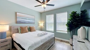 Ein Schlafzimmer mit einem Bett, Nachttischlampen, einem Deckenventilator, einem Fenster mit Jalousien und einer Pflanze.