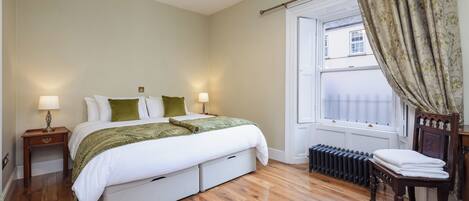 A bedroom with a bed, bedside tables, a radiator, a window with curtains, and a chair.