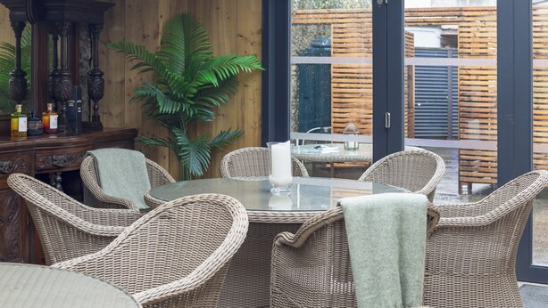 A wicker dining area with a glass table, chairs, and a potted plant.