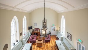 A spacious room with high ceilings, arched windows, a chandelier, and a fireplace.
